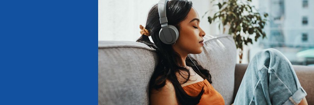 Une jeune femme est assise sur un canapé. Elle a les yeux fermés et un casque sur les oreilles