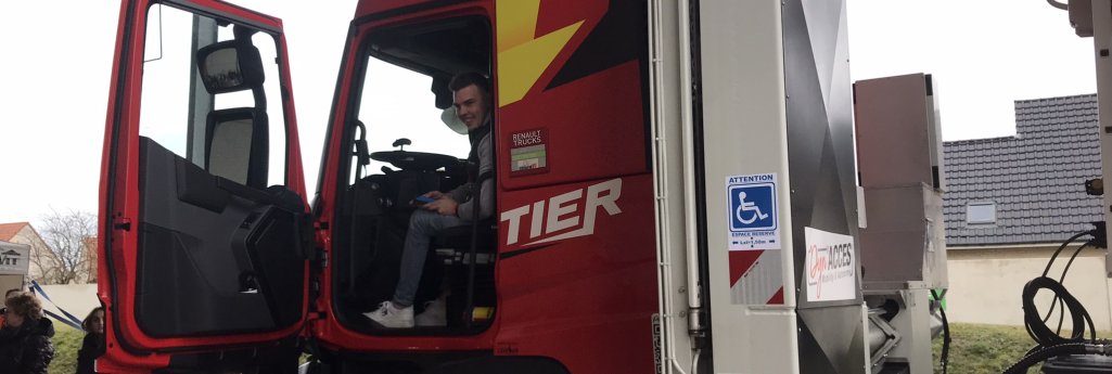 Jérémy est assis dans la cabine de son camion. Une plateforme élévatrice plié est présente derrière avec le sigle personne à mobilité réduite est visible.