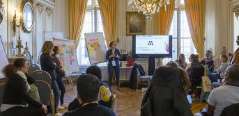 Un atelier lors de l'URRH dans un des salons du Palais de la Bourse à Bordeaux. Une animatrice est debout devant de nombreuses personnes assises qui la regardent et l'écoutent.