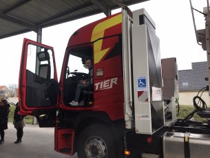 Jérémy est assis dans la cabine de son camion. Une plateforme élévatrice plié est présente derrière avec le sigle personne à mobilité réduite est visible.