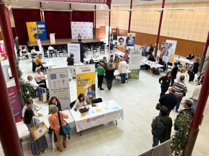La photo prise en contre-haut montre en premier plan la salle où se trouve une dizaine de stands et en fond la scène qui accueille les conférences.