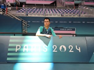 Michel pose devenat un panneau vert et blanc sur lequel est inscrit Paris 2024