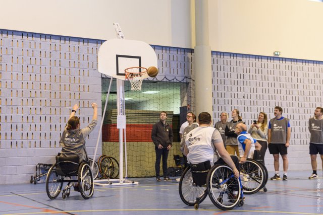 L'équipe grise et l'équipe blanche s'affrontent au basket fauteuil. La joueuse de l'équipe grise shoote et le ballon passe à côté de l'arceau