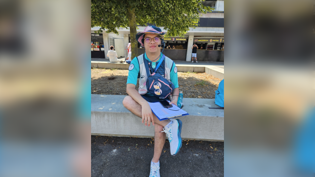 Michel est assis sur un banc muni d'un micro casque et d'unefeuille de route afin d'informer les spectateurs
