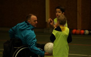 Un éducateur tient un ballon et parle à deux jeunes sportifs