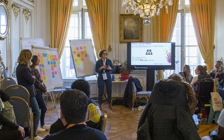 Un atelier lors de l'URRH dans un des salons du Palais de la Bourse à Bordeaux. Une animatrice est debout devant de nombreuses personnes assises qui la regardent et l'écoutent.