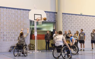 L'équipe grise et l'équipe blanche s'affrontent au basket fauteuil. La joueuse de l'équipe grise shoote et le ballon passe à côté de l'arceau