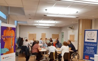 Des référents handicap réunis sur 3 tables espacées travaillent en sous-groupe sur un atelier. A gauche de la photo, se trouve un roll'up Agefiph représentant une femme tenant l'inscription Talent Handicap. A droite de l'image un roll up du Comité Départemental Olympique et Sportif est positionné. Il est de couleur bleu et blanche avec le logo représentant les anneaux et un coq et l'adresse.