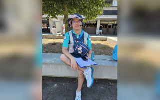 Michel est assis sur un banc muni d'un micro casque et d'unefeuille de route afin d'informer les spectateurs
