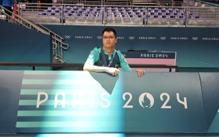 Michel pose devenat un panneau vert et blanc sur lequel est inscrit Paris 2024